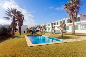 Una piscina rodeada de césped, palmeras y un edificio con múltiples ventanas y balcones.