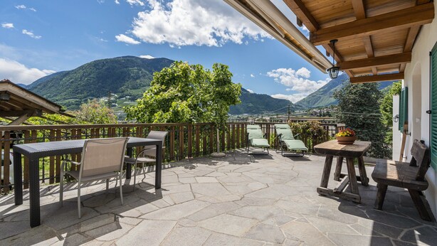 Eine Terrasse mit Steinböden, Holzmöbeln und Bergblick.
