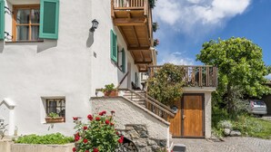 Ein traditionelles Gebäude mit einer Steinstufen-Treppe, einem hölzernen Balkon und einem kleinen Garten mit roten Blüten.