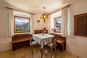 A dining area with a wooden bench, a table with a tablecloth, and two windows with curtains.