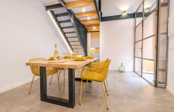 Un coin repas avec une table en bois, des chaises jaunes, une bouteille de vin et un vase.