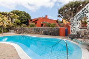 A swimming pool with a stone wall and a red building in the background.