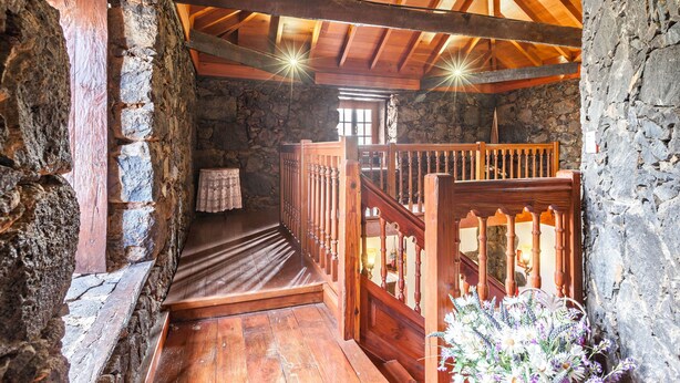 Ein rustikales Steininnere mit einer Holztreppe, Holzwandläufen und einem kleinen Tisch mit einer Decke.