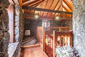 A rustic stone interior with a wooden staircase, wooden railings, and a small table with a cloth.
