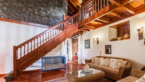 Ein geräumiger Wohnbereich mit einer Holztreppe, einem Korbsessel, einem Glastisch und einer Steinwand.