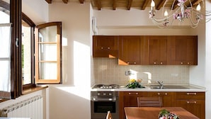 A kitchen with wooden cabinets, a stove, and a dining table with fruit. - Villa Ornata B: A characteristic and welcoming apartment surrounded by the greenery, with Free WI-FI. (Cannara)