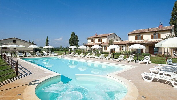 A swimming pool with lounge chairs and umbrellas, surrounded by buildings with tiled roofs and a clear sky. - Villa Ornata B: A characteristic and welcoming apartment surrounded by the greenery, with Free WI-FI. (Cannara)