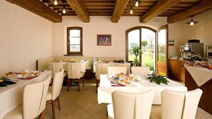 A dining area with wooden beams, white tables, and chairs. There are windows with views of greenery outside. - Villa Ornata B: A characteristic and welcoming apartment surrounded by the greenery, with Free WI-FI. (Cannara)