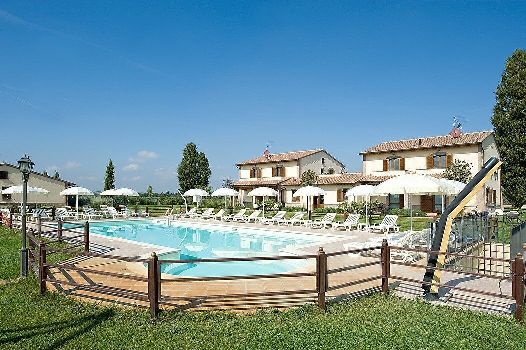A swimming pool with lounge chairs and umbrellas, surrounded by a wooden fence.