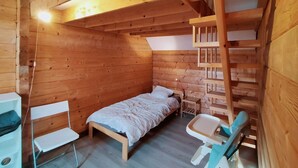 A wooden cabin room with a bed, a desk, and a chair.