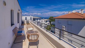 A balcony with wicker chairs and a table, overlooking a coastal area with buildings and a clear sky. - Apartment LAGANINI I near the beach (Njivice)