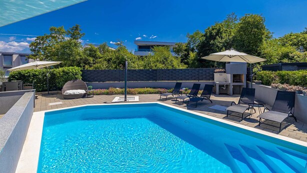 A swimming pool with lounge chairs and umbrellas, surrounded by a landscaped garden and a brick wall. - Apartment LAGANINI I near the beach (Njivice)