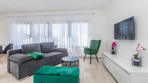 A modern living room with a grey sofa, a green armchair, a round coffee table, and a TV mounted on the wall. - Apartment LAGANINI I near the beach (Njivice)