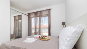 A hotel room with a bed, a window with curtains, a bedside table with a tray of fruit, and a lamp. - Apartment LAGANINI I near the beach (Njivice)