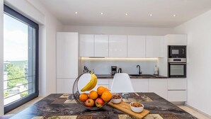 Una cocina moderna con armarios blancos, horno integrado y microondas. Un frutero con plátanos, naranjas y manzanas está sobre la encimera.