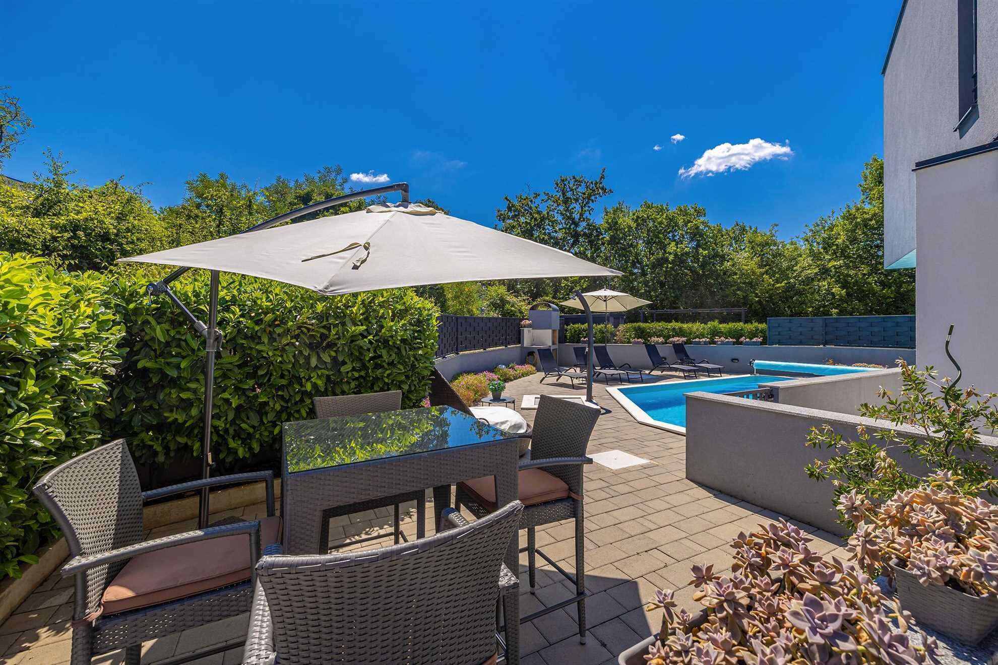 A backyard with a swimming pool, outdoor furniture, and a large umbrella.