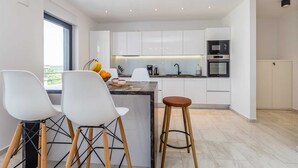 Una cocina moderna con gabinetes blancos, una isla central y un comedor con sillas blancas.