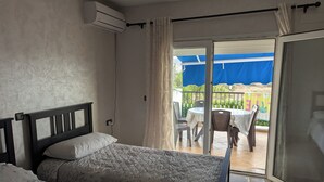 A hotel room with two beds, a balcony with a table and chairs, and an air conditioning unit on the wall. - 2 Bed Flat - Sleeps 5 - Pets - Pool - Parking (Saidia)