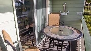 Een overdekt terras met een ronde tafel en stoelen, een schuifdeur en een kleine ankerdecoratie aan de muur.