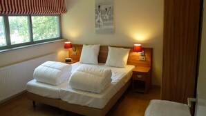 Une chambre à coucher avec un lit, deux tables de chevet, une fenêtre donnant sur un paysage agréable et une porte.