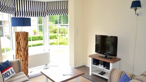 Un salon comprenant un téléviseur, un canapé, une table basse et une grande fenêtre donnant sur un paysage verdoyant.