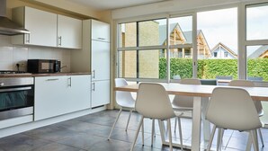 Une cuisine moderne avec des meubles blancs, une cuisinière et un coin repas comprenant une table et des chaises.