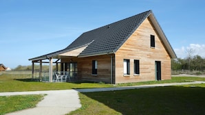 Une maison moderne en bois, dotée d’un toit à pente, d’un porche couvert et d’une porte en verre transparent.