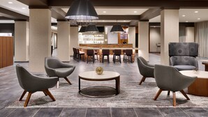 A modern lobby with grey upholstered chairs, a central round table, and a bar area in the background. - Courtyard by Marriott Atlanta Duluth Downtown (Duluth)