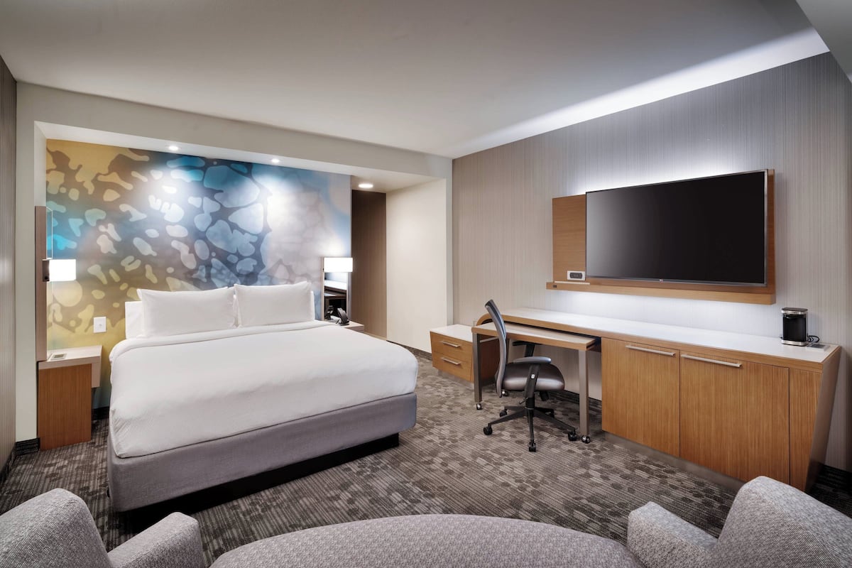 Een hotelkamer met een groot bed, een bureau met stoel, een flatscreen-tv en een decoratief muurschildering.