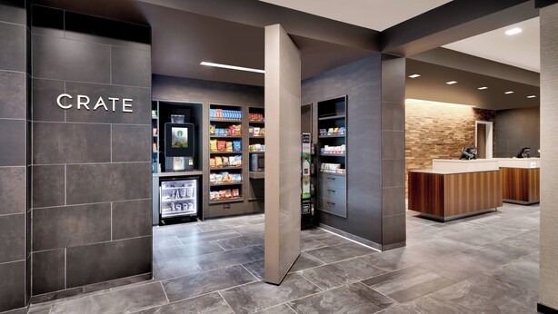 A modern interior with a 'CRATE' sign, self-service beverage machines, and a reception area with a wooden counter. - Courtyard by Marriott Atlanta Duluth Downtown (Duluth)