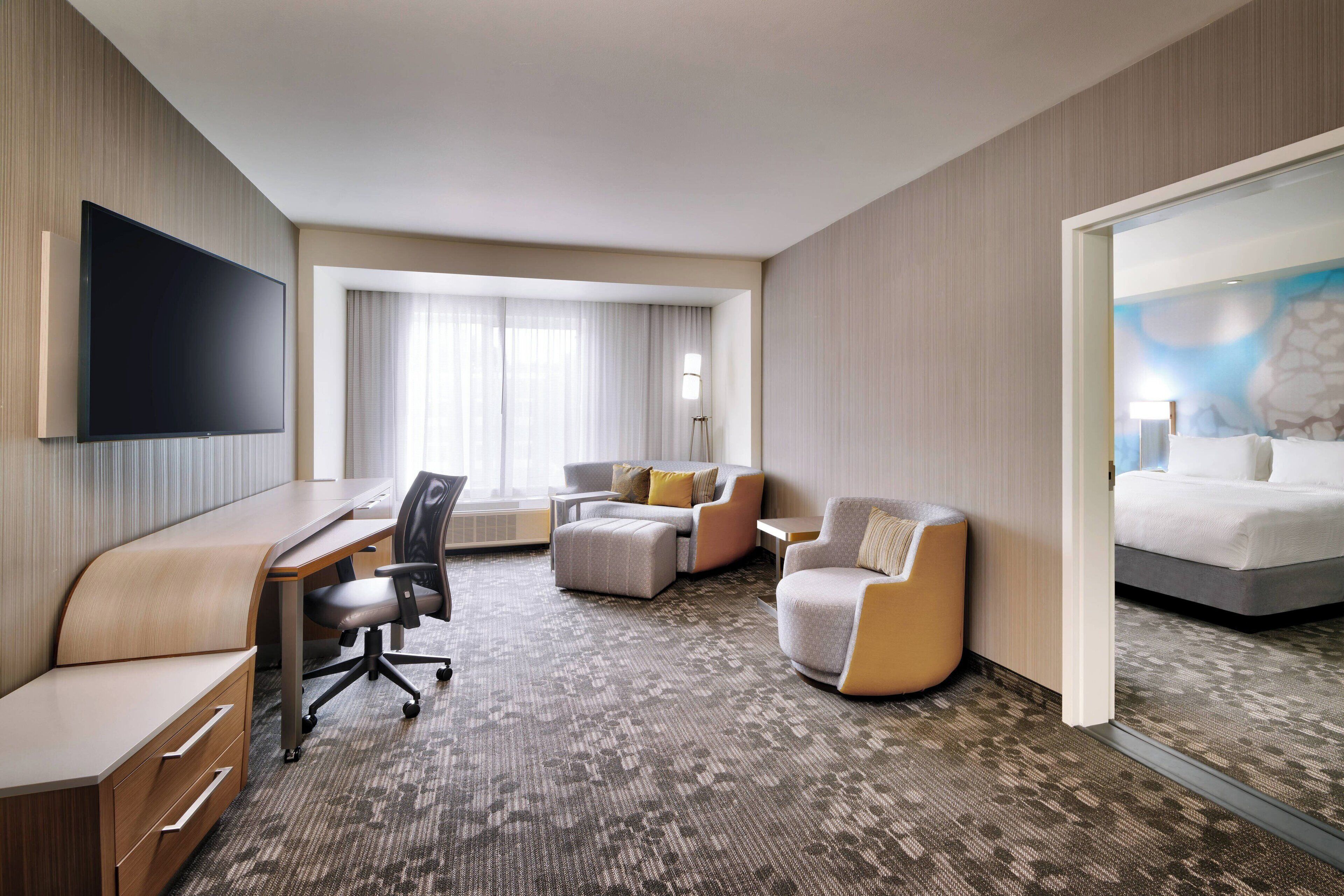 Habitación de hotel con televisión de pantalla plana, escritorio, zona de estar confortable con sofá y sillones, cama y ventana grande con cortinas.