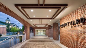 A hotel entrance with a brick facade, a sign reading "Courtyard by Marriott," and a view of a building with a clock tower in the background. - Courtyard by Marriott Atlanta Duluth Downtown (Duluth)