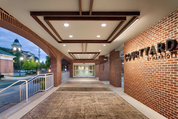 L’entrée d’un hôtel avec une façade en briques, une enseigne indiquant « Courtyard by Marriott », et, au loin, une vue sur un bâtiment doté d’une tour horloge.