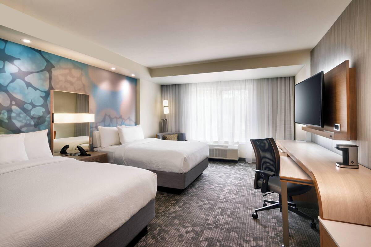Een hotelkamer met twee bedden, een bureau, een flatscreen televisie, een groot raam met gordijnen, en een muurschildering.