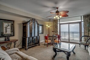 A living room with a large wooden cabinet, a glass coffee table, and a ceiling fan. - Gorgeous 16th Floor Oceanfront Condo at North Beach Resort & Villas - $300 FREE Activities Daily! (North Myrtle Beach)