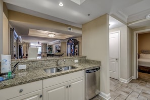 Kitchen features a large mirror above the sink and a ceiling light fixture, with a door leading to a bedroom with a bed.