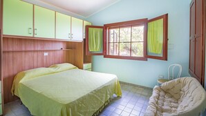 Ein Zimmer mit einem Bett, einem Sessel und einem Fenster mit Vorhängen.