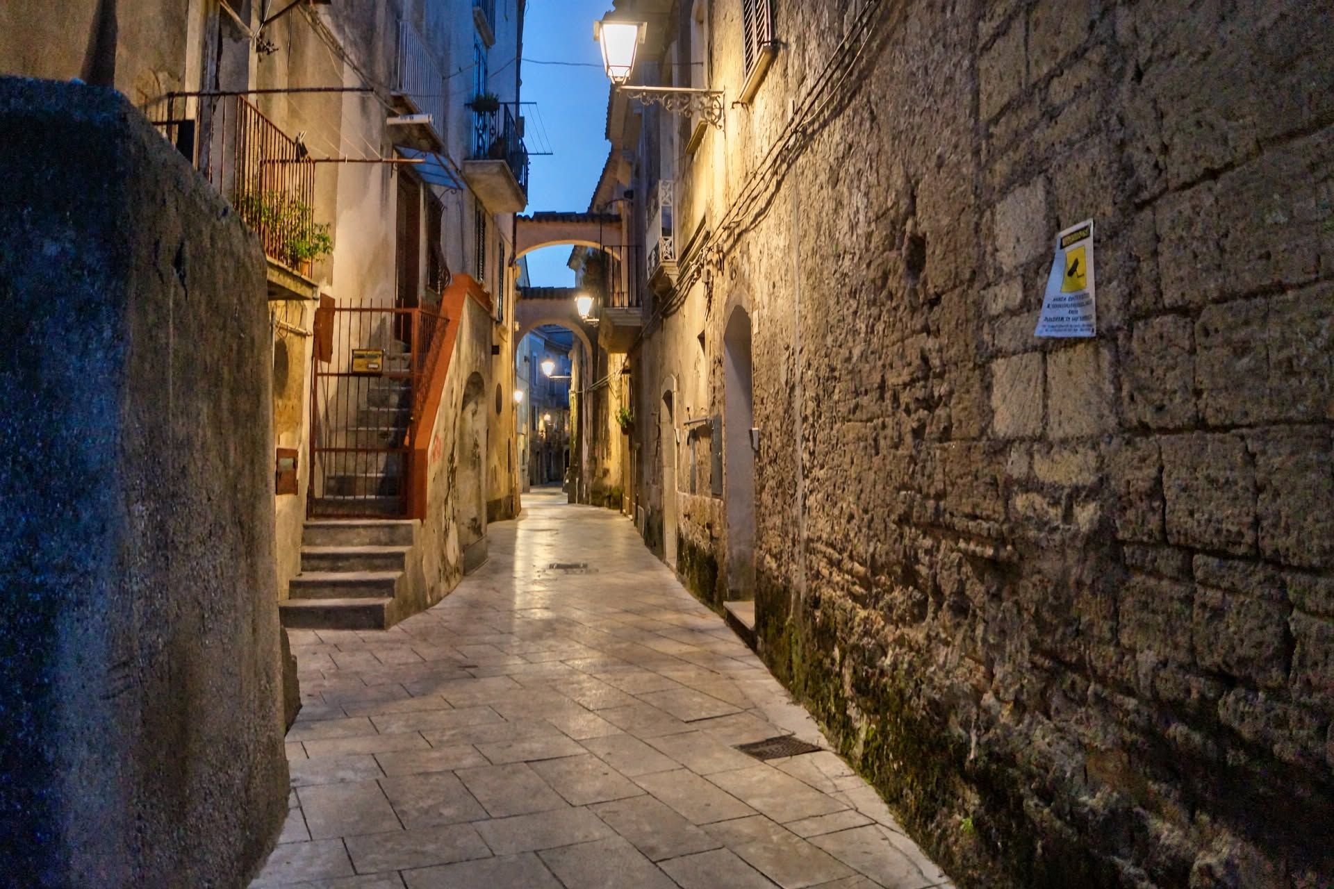Une rue étroite bordée de murs en pierre, avec un escalier et un panneau indiquant une zone piétonne.