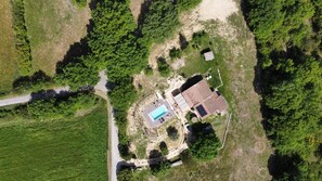An aerial view of a property with a swimming pool, a large building with a tiled roof, and surrounding greenery.