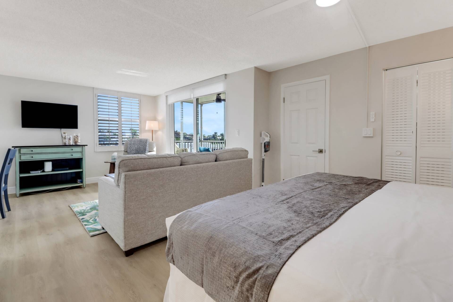 Ein Hotelzimmer mit Bett, Sofa, Fernseher, Schreibtisch und einem Balkon mit Aussicht.