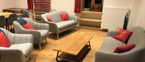 Un salón con sofás y sillones grises, una mesa de centro de madera y un radiador.