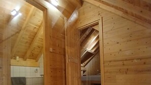 Ein Holzinnenraum mit schrägverdeckelter Decke, einem sichtbaren Badezimmer mit gefliestem Wandbereich und einer Holztür.