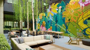 An outdoor seating area with a sofa, chairs, and tables, surrounded by greenery and a colorful mural. - Bellyard, West Midtown Atlanta, a Tribute Portfolio Hotel (Atlanta)