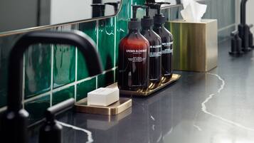 Una encimera de baño con tres botellas de crema corporal 'Grown Alchemist', un dispensador de jabón y una caja de pañuelos.