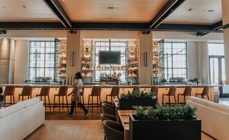 Un área de bar moderna con una barra larga, varios taburetes y una variedad de botellas y vasos.