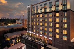 Un hotel de varios pisos con diseño moderno, que destaca un letrero 'BELLYARD', un área de patio en la azotea con asientos al aire libre y un horizonte urbano de fondo.