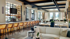 A modern bar area with a long counter, multiple bar stools, and a television screen. There is a seating area with a sofa and chairs, and a coffee table with decorative items. - Bellyard, West Midtown Atlanta, a Tribute Portfolio Hotel (Atlanta)