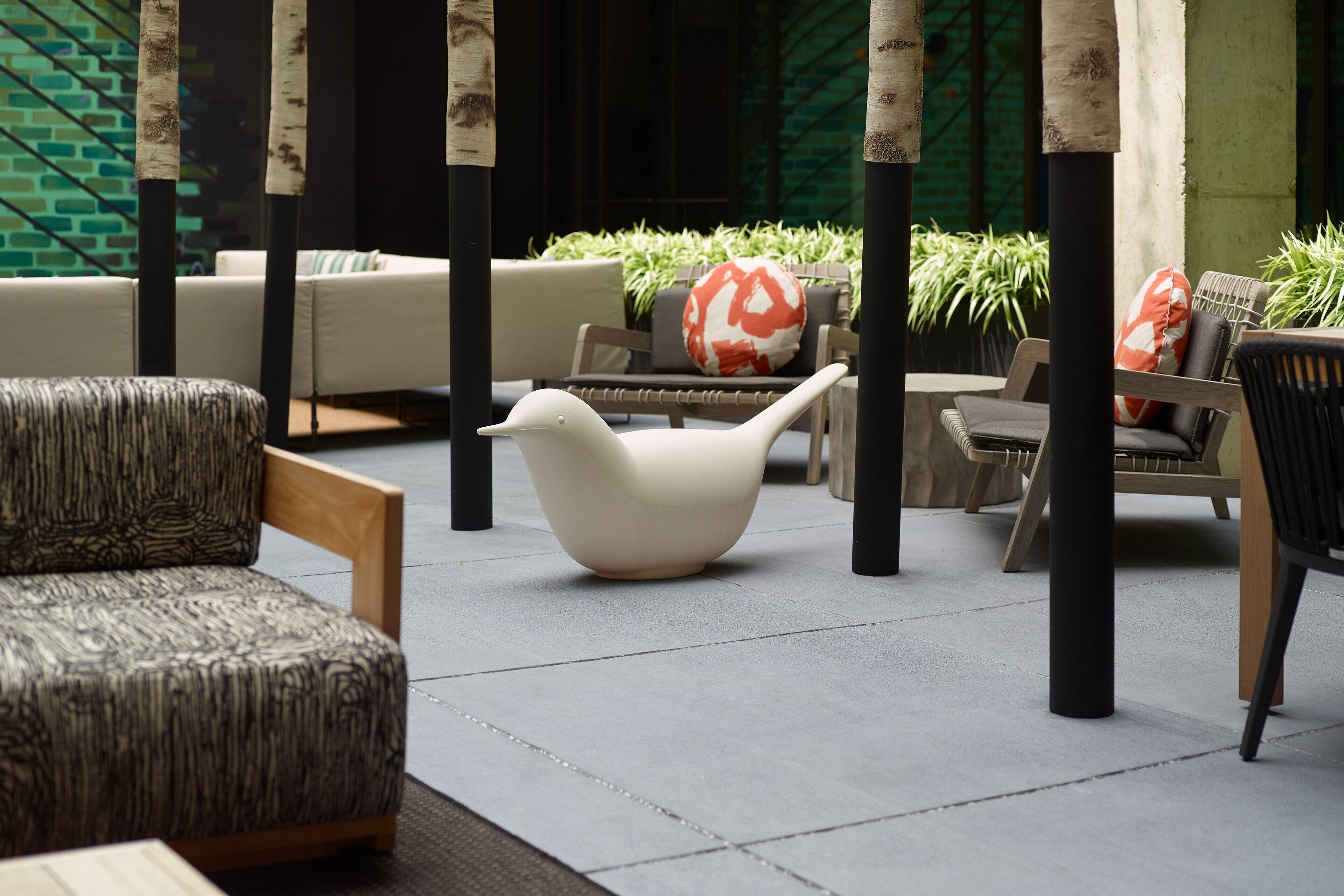 A modern outdoor seating area with a white bird-shaped chair, cushioned sofas, and wooden chairs.