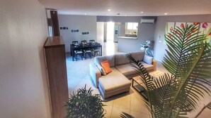 Een moderne woonkamer met een bank, eettafel en stoelen. Achtergrond toont een keukenhoek.