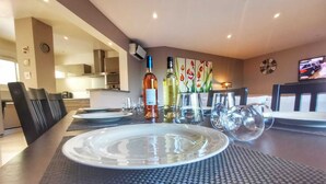 Een eettafel gedekt met borden, glazen en flessen, met een keuken en zithoek op de achtergrond.